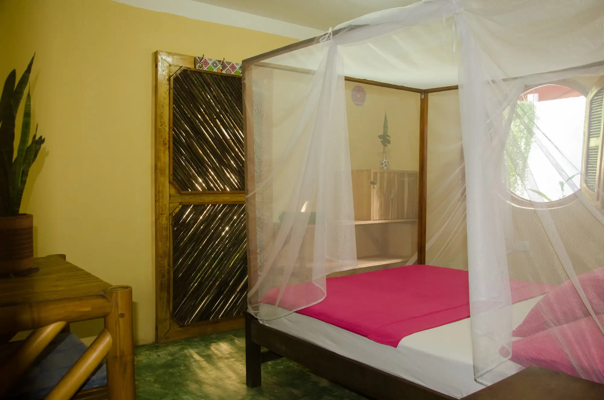 La cama doble bajo su toldillo de cuatro postes, junto a la puerta de madera y la ventana redonda.