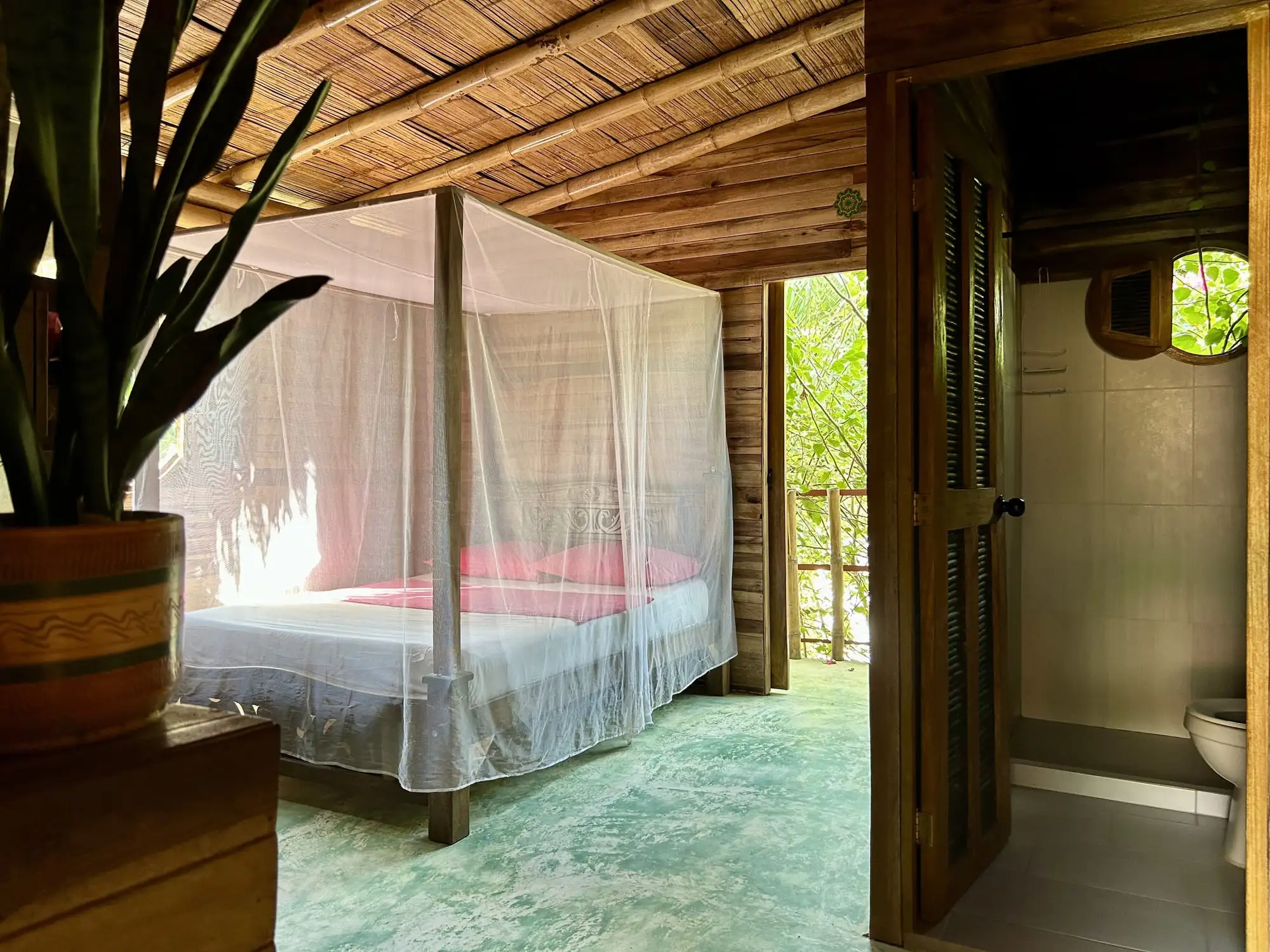 La habitación familiar de madera con la cama doble bajo toldillo y la puerta abierta del baño privado.