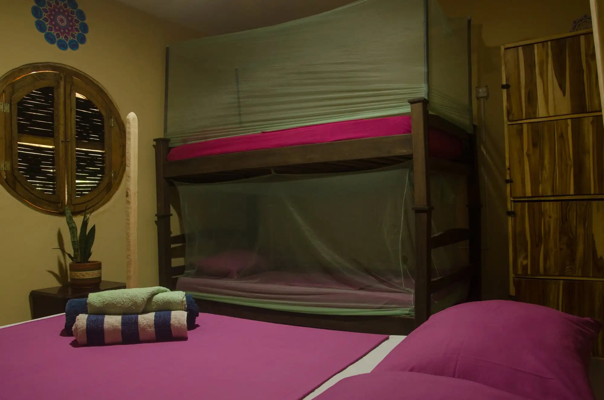 Habitación familiar de paredes amarillas con una cama doble adelante y un camarote de madera con toldillos atrás.